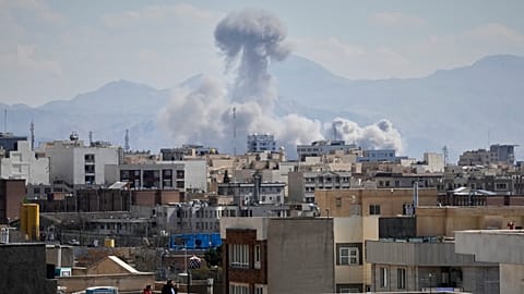 People watch from a rooftop as a plume of smoke rises after a strike in Tehran, Iran, Sunday, March 1, 2026. (