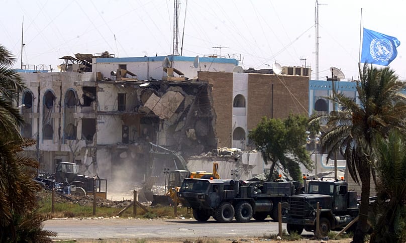 Veículos militares americanos passam pela secção desmoronada da sede das Nações Unidas em Bagdade, 23 de agosto de 2003 