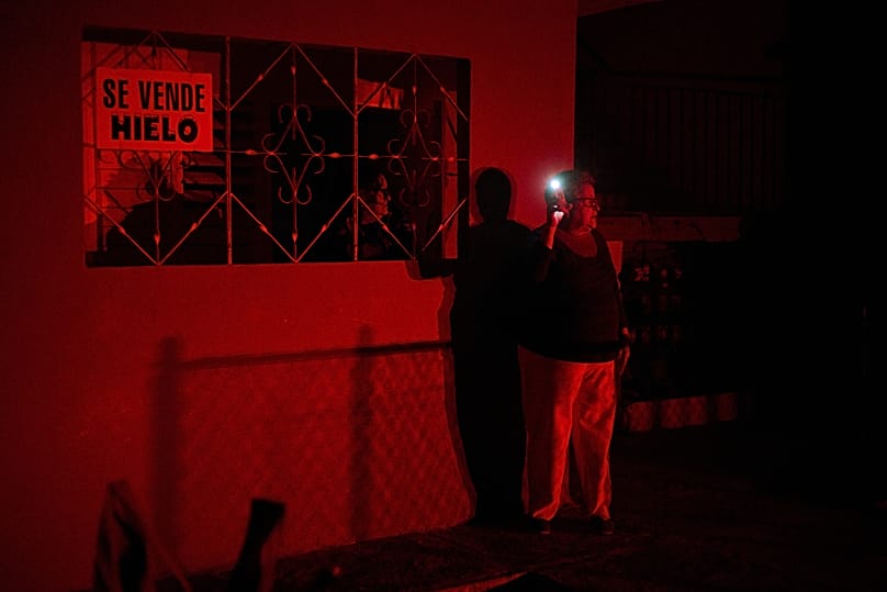 Una mujer con la luz del móvil encendida, enfrente de un cartel que reza "se vende hielo".