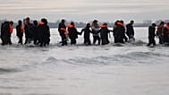 Migrants walk in the water to board a small boat in an attempt to reach Britain