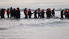 Migranten waten durchs flache Meer zu einem kleinen Boot, um von dort aus nach Großbritannien überzusetzen.