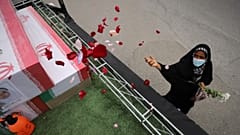 Minab'daki kız ilkokulunda hayatını kaybedenlerin tabutlarının üzerine bir kadın gül yaprakları serpiyor.