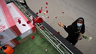 Minab'daki kız ilkokulunda hayatını kaybedenlerin tabutlarının üzerine bir kadın gül yaprakları serpiyor.