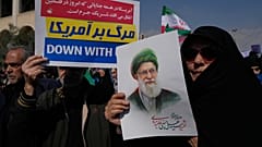 امرأة تحمل صورة للمرشد الإيراني الراحل آية الله علي خامنئي، بينما يرفع رجل لافتة مكتوب عليها بالفارسية: الموت لأمريكا