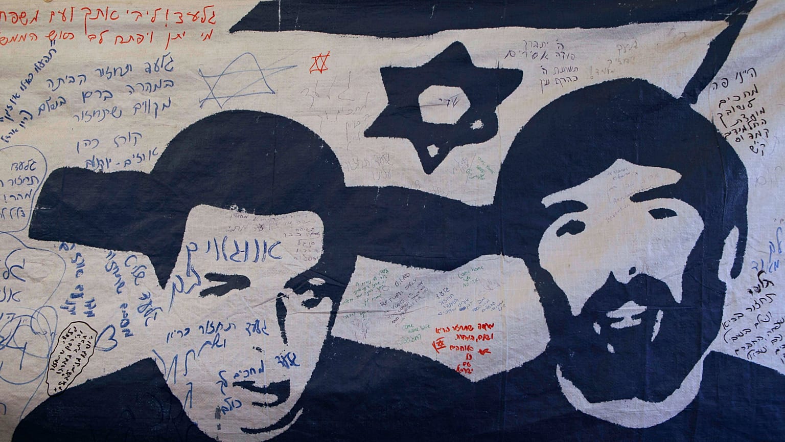 ملصق يحمل صور الجندي في الجيش الإسرائيلي الرقيب جلعاد شاليط (يسارًا) والملاح الجوي في سلاح الجو الإسرائيلي رون آراد (يميناً).