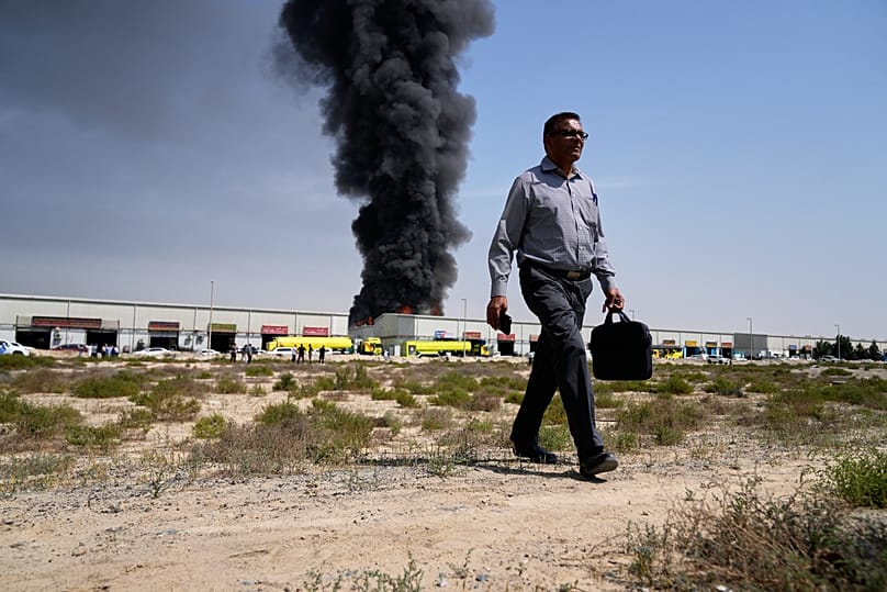 A man walks away after watching a black plume of smoke rising from a warehouse in the industrial area of Sharjah City, 1 March, 2026