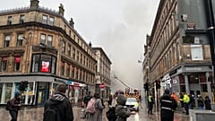 Menschen beobachten aufsteigenden Rauch. Feuerwehrleute löschen die letzten Glutnester in einem ausgebrannten Gebäude.