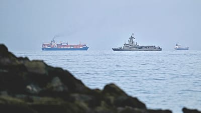 A UAE navy ship sails next to a cargo ship in the Strait of Hormuz as seen from Khor Fakkan, United Arab Emirates, Wednesday, March 11, 2026. 