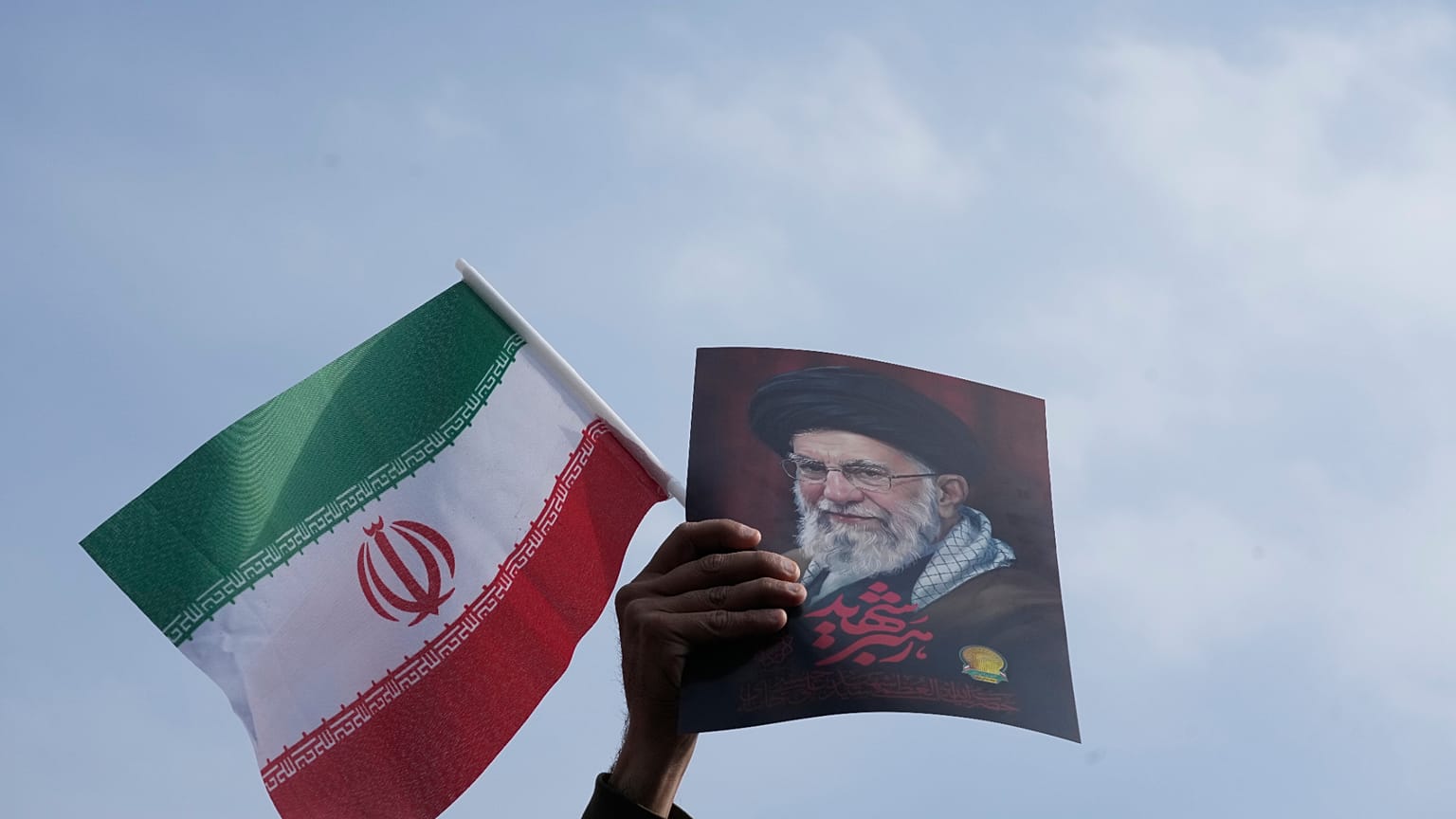 رجل يرفع علم إيران وملصقاً للمرشد الأعلى الراحل آية الله علي خامنئي خلال مهرجان دعم لابنه، آية الله مجتبى خامنئي، الذي خلف والده كمرشد أعلى جديد