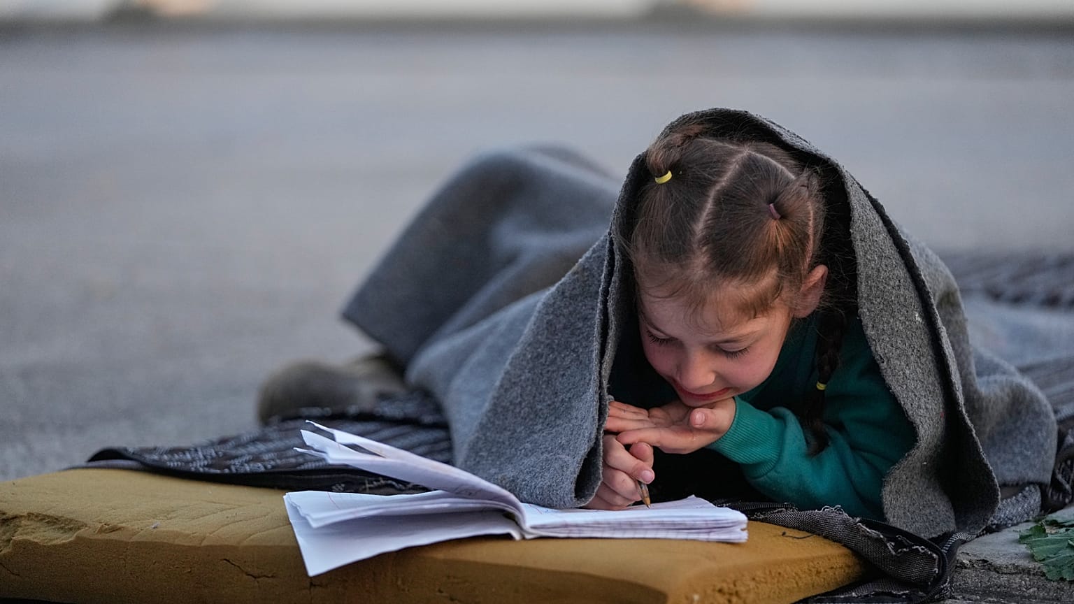 İsrail hava saldırıları nedeniyle yerinden edilen 7 yaşındaki Hanaa, 6 Mart 2026 Cuma günü Lübnan'ın başkenti Beyrut'ta yolda battaniyeye sarınarak defterine bir şeyler yazıyor