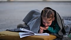 İsrail hava saldırıları nedeniyle yerinden edilen 7 yaşındaki Hanaa, 6 Mart 2026 Cuma günü Lübnan'ın başkenti Beyrut'ta yolda battaniyeye sarınarak defterine bir şeyler yazıyor