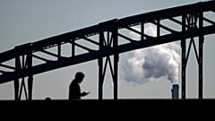 Ein Mann geht über eine Brücke und schaut auf sein Handy; im Hintergrund steigt Rauch aus einer Müllverbrennungsanlage nahe Paris auf, am Donnerstag, 23. September 2021.