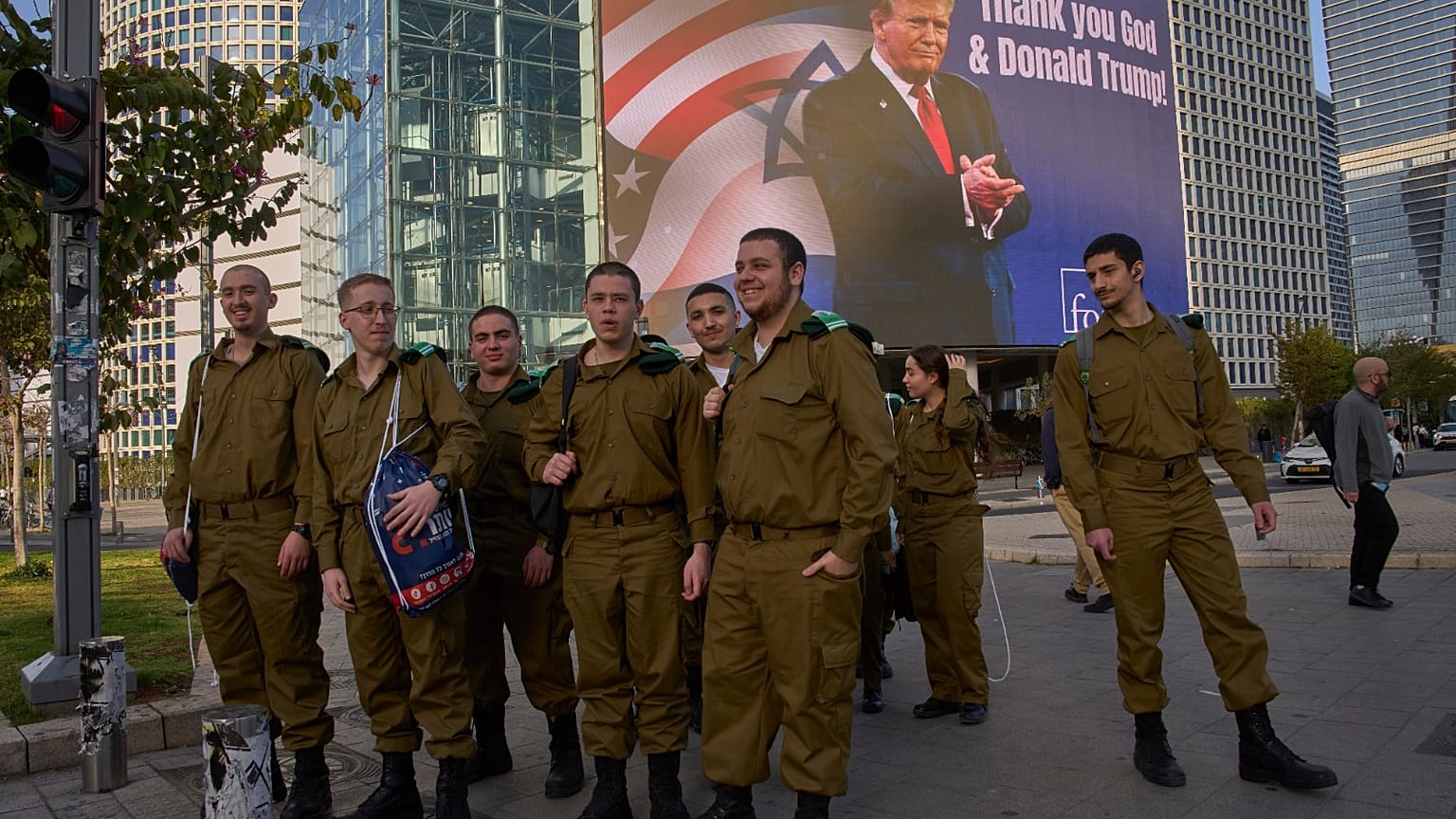 جنود إسرائيليون يمرون بلوحة إعلانية إلكترونية تعرض صورة الرئيس دونالد ترامب إلى جانب رسالة "الحمد لله ودونالد ترامب" في إشارة إلى تورط أمريكا في الحرب بين إسرائيل وإيران 2026