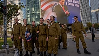 جنود إسرائيليون يمرون بلوحة إعلانية إلكترونية تعرض صورة الرئيس دونالد ترامب إلى جانب رسالة "الحمد لله ودونالد ترامب" في إشارة إلى تورط أمريكا في الحرب بين إسرائيل وإيران 2026