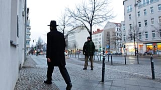  صورة التُقطت في 12 مارس/آذار 2010 تُظهر رجلاً يهودياً أرثوذكسياً من طائفة لاودر يشورون يمر بجانب شرطي أثناء دخوله كنيساً محروساً في برلين