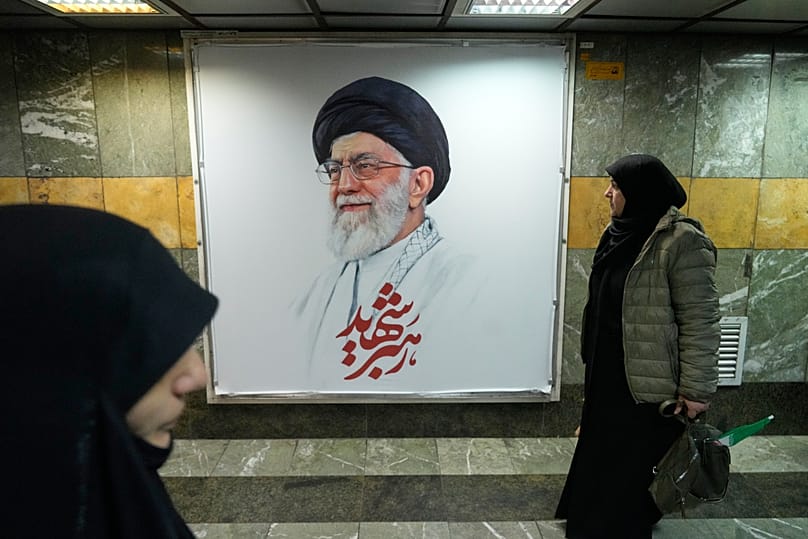 People walk past a portrait of the late Iranian Supreme Leader Ayatollah Ali Khamenei in a subway station in Tehran, 13 March, 2026