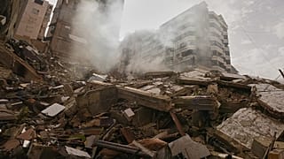 A man stands atop the rubble of a building destroyed in an Israeli airstrike as a bulldozer clears debris in Dahiyeh, 14 March, 2026