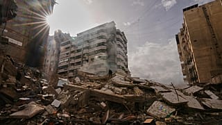 A man stands atop the rubble as smoke rises from a building destroyed in an Israeli airstrike in Dahiyeh, 14 March, 2026