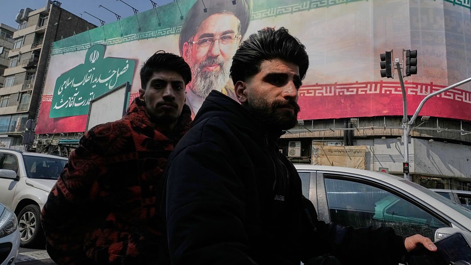 رجلان يركبان دراجتهما النارية أمام لوحة إعلانية للمرشد الأعلى الإيراني آية الله مجتبى خامنئي في وسط مدينة طهران، إيران، السبت 14 مارس 2026.