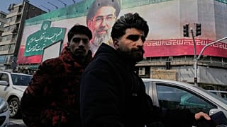 رجلان يركبان دراجتهما النارية أمام لوحة إعلانية للمرشد الأعلى الإيراني آية الله مجتبى خامنئي في وسط مدينة طهران، إيران، السبت 14 مارس 2026.