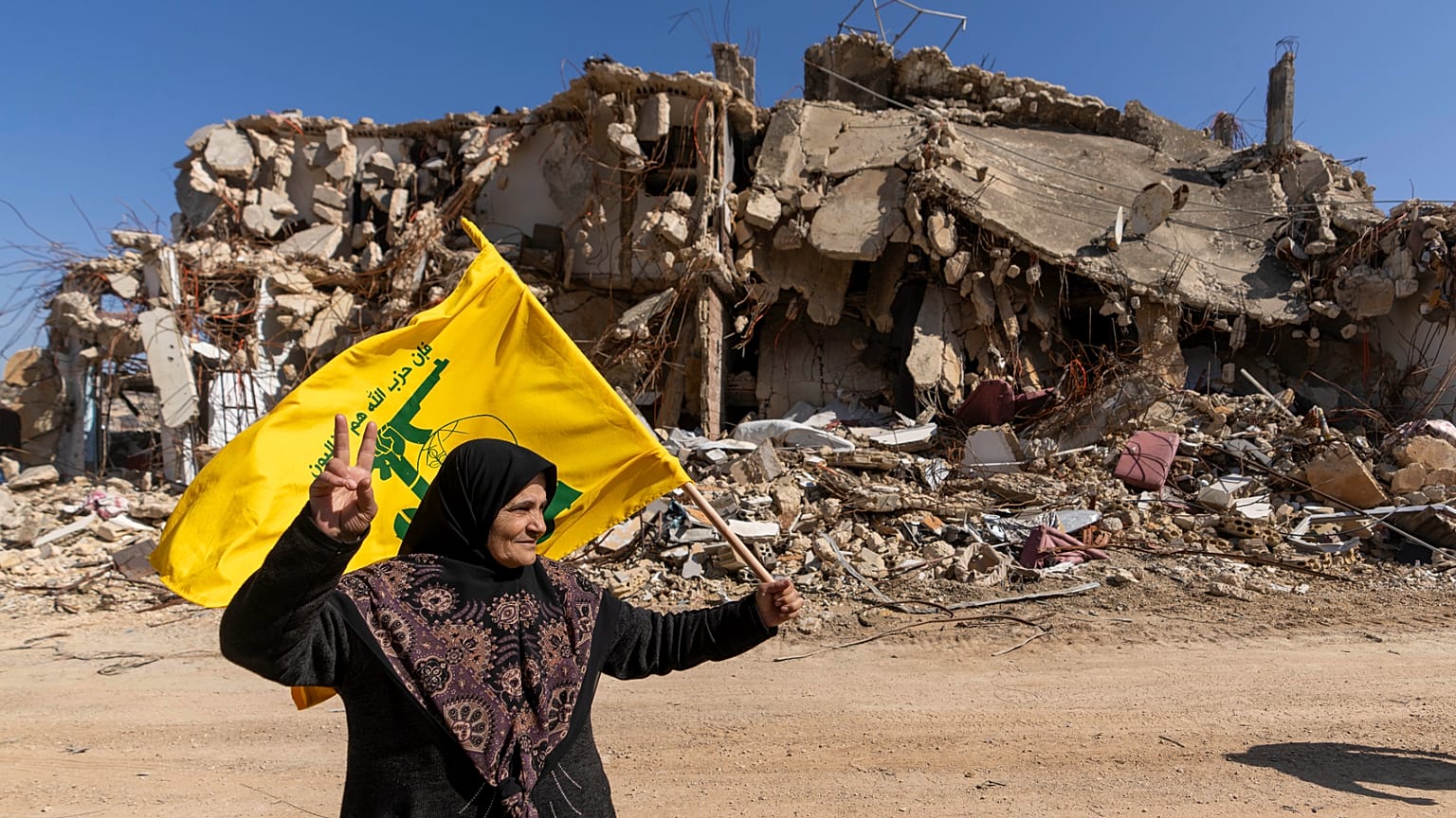  لبنانية تحمل علم حزب الله في قريتها التي دمرتها الحرب الإسرائيلية في كفركلا جنوب لبنان، الثلاثاء 18 فبراير/شباط 2025.