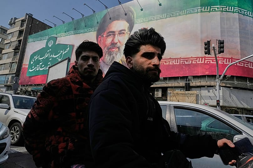 Two men ride their motorbike past a billboard of the Iranian Supreme Leader Ayatollah Mojtaba Khamenei in downtown Tehran, Iran, Saturday, March 14, 2026