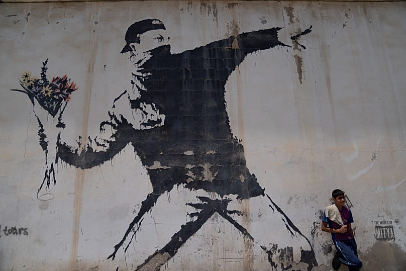 Ein palästinensischer Arbeiter ruht unter einem Wandgemälde von Banksy an einer Tankstelle in Bethlehem im Westjordanland - 2022