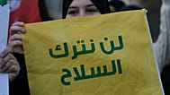 أحد أنصار حزب الله تحمل علمًا عليه رسالة باللغة العربية: "لن نلقي السلاح"