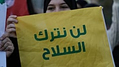 أحد أنصار حزب الله تحمل علمًا عليه رسالة باللغة العربية: "لن نلقي السلاح"