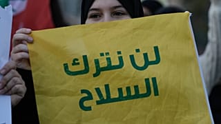 أحد أنصار حزب الله تحمل علمًا عليه رسالة باللغة العربية: "لن نلقي السلاح"