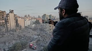 رجل يسجل المشهد على هاتفه بينما يبحث عمال الإنقاذ بين أنقاض مبنى دمر في غارة جوية إسرائيلية في وسط بيروت، لبنان، الأربعاء 18 مارس 2026.