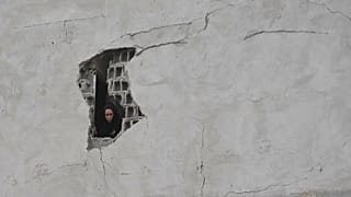 A woman looks through a damaged wall of a residential building after a nearby police station was struck in Tehran, 15 March, 2026