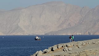 Um casal de turistas contempla as montanhas a sul do Estreito de Ormuz, enquanto navios estão atracados nas águas do Golfo Pérsico, perto da cidade de Khasab, em Omã