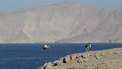 Um casal de turistas contempla as montanhas a sul do Estreito de Ormuz, enquanto navios estão atracados nas águas do Golfo Pérsico, perto da cidade de Khasab, em Omã