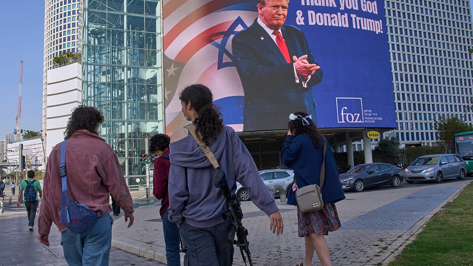 يمر الناس أمام لوحة إعلانية إلكترونية تعرض صورة الرئيس دونالد ترامب إلى جانب رسالة "الحمد لله ودونالد ترامب" في إشارة إلى تورط أمريكا في الحرب بين إسرائيل وإيران