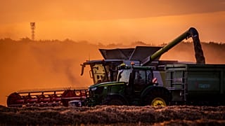 Una máquina siega un campo en Alemania con el sol iniciando la puesta.