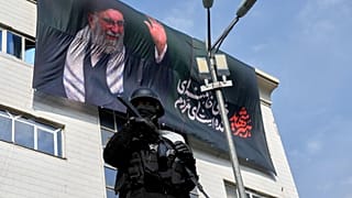 يقف ضابط أمن حارساً خلال مظاهرة لدعم مجتبى خامنئي، كمرشد أعلى، مع ظهور لوحة إعلانية لعلي خامنئي في الخلفية، في طهران، إيران، يوم الاثنين 9 مارس 2026. 