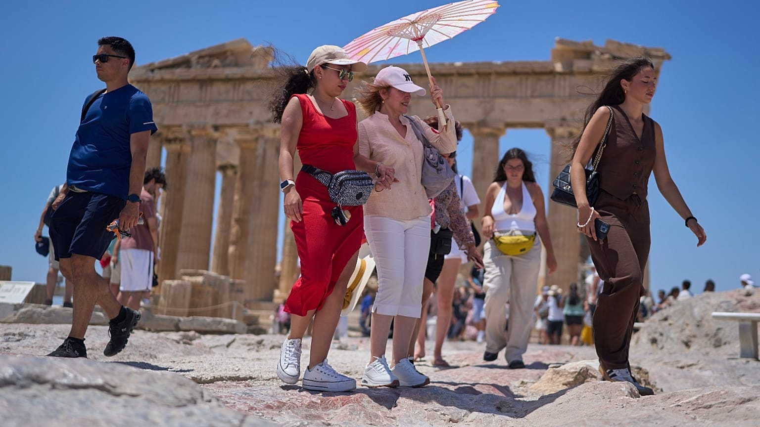 تجول السياح بالمظلة أمام معبد البارثينون القديم في تلة الأكروبوليس، الخميس 26 يونيو 2025، مع وصول أول موجة حر صيفية إلى اليونان، حيث من المتوقع أن تتجاوز درجات الحرارة 40 درجة
