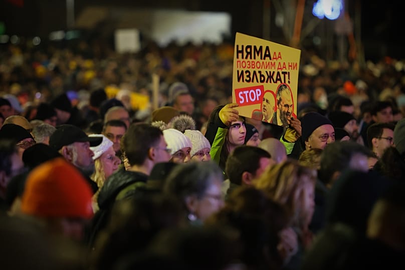 Manifestante segura um cartaz com as frases «Não vamos deixar que nos enganem» e «Apenas voto eletrónico», numa manifestação nas ruas de Sófia. 14 janeiro 2026