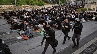 عناصر من الشرطة الإسرائيلية يمرّون قرب مصلّين فلسطينيين يؤدّون صلاة عيد الفطر بالقدس، في 20 مارس 2026.