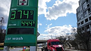 Üzemanyagárak egy benzinkút tábláján, 2026. március 17-én az egyesült államokbeli Baltimore-ban, miközben egy üzemanyag-szállító teherautó elhalad mellettük