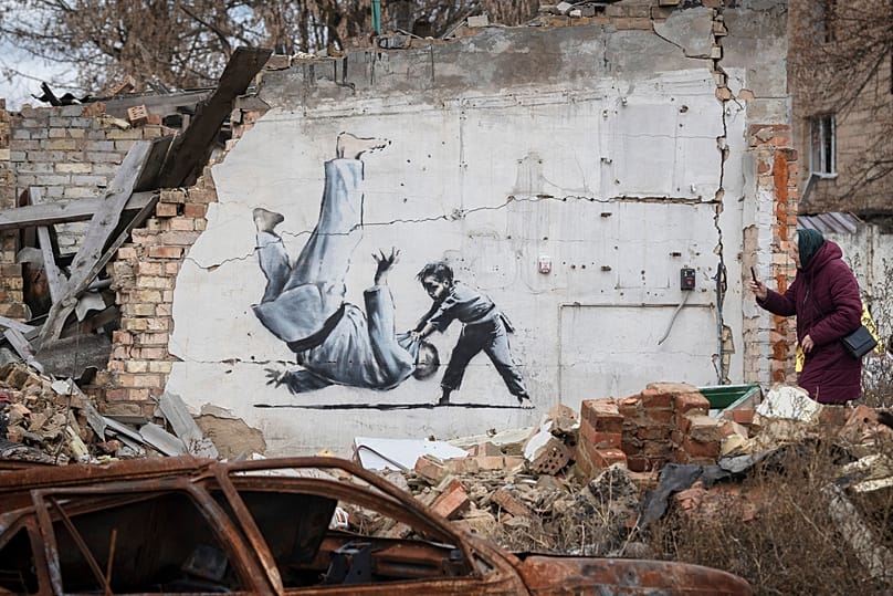 Gemini şunu dedi: Ukrayna Borodyanka’da bir kadın, yıkık bir binada Banksy’ye ait olduğu düşünülen eserin fotoğrafını çekiyor. 
