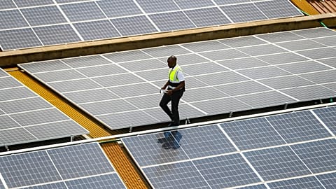 FILE - Mark Munyua, CP solar's technician, examines solar panels on the roof of a company in Nairobi, Kenya, Sept. 1, 2023. 