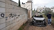 رجل فلسطيني يتفقد مركبة أُحرقت إلى جانب كتابة بالعبرية تعني "انتقام"، بعد هجوم لمستوطنين على قرى قرب نابلس، في دير الحطب، في 23 مارس 2026.