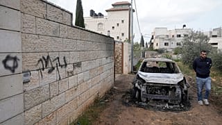 رجل فلسطيني يتفقد مركبة أُحرقت إلى جانب كتابة بالعبرية تعني "انتقام"، بعد هجوم لمستوطنين على قرى قرب نابلس، في دير الحطب، في 23 مارس 2026.