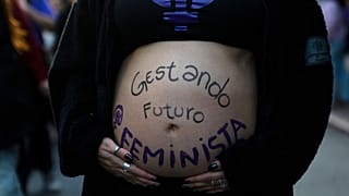 Uma mulher participa numa marcha feminista com a barriga pintada com uma mensagem.