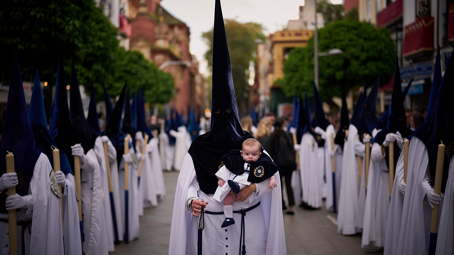 Un penitente sostiene a su hijo de seis meses durante una procesión de Semana Santa en Sevilla, España, el domingo 13 de abril de 2025.