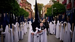 Un penitente sostiene a su hijo de seis meses durante una procesión de Semana Santa en Sevilla, España, el domingo 13 de abril de 2025.