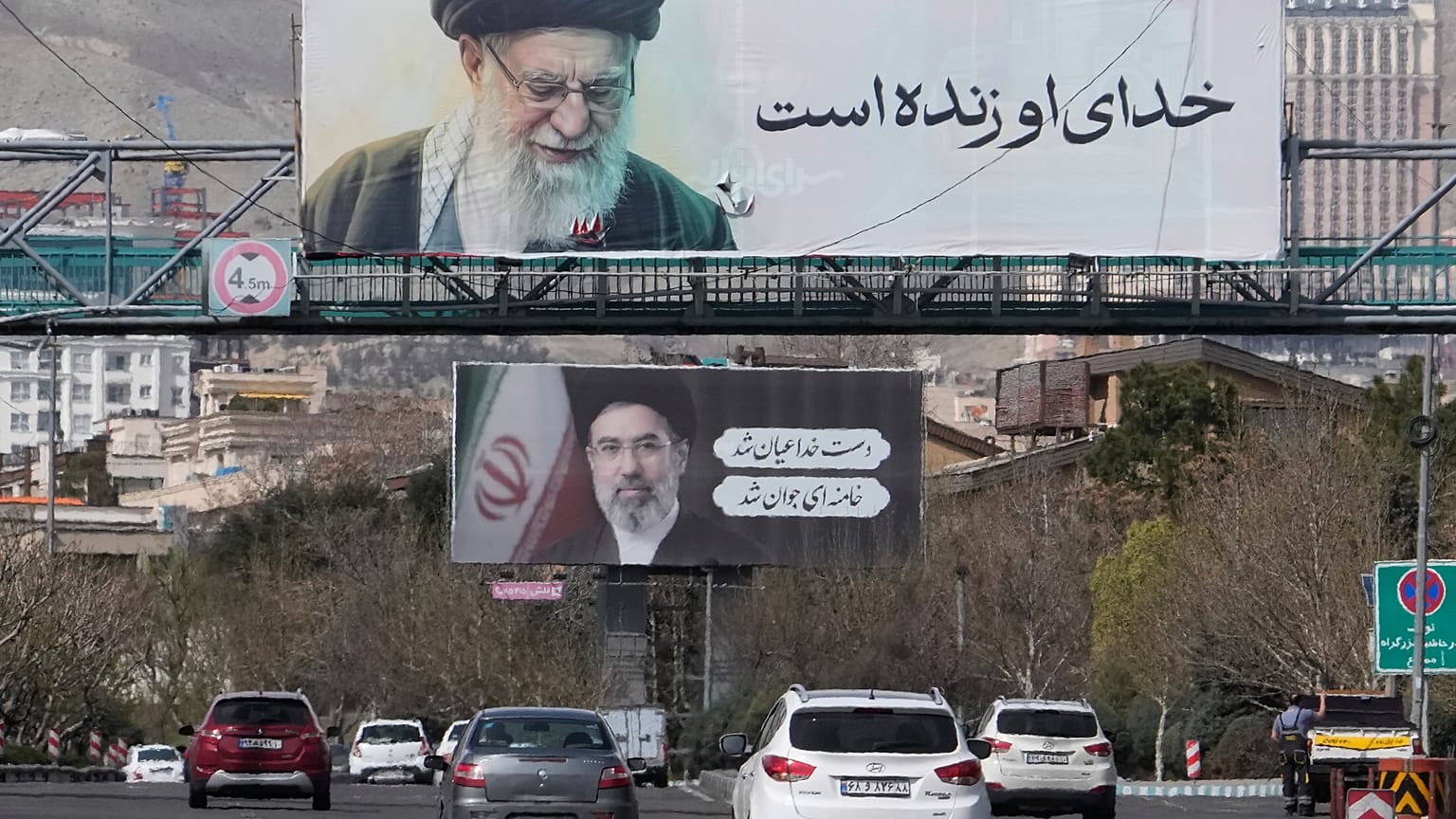 تسير المركبات تحت لوحات إعلانية تظهر صور المرشد الأعلى الإيراني الراحل آية الله علي خامنئي، في المقدمة، وابنه آية الله مجتبى خامنئي، خليفته