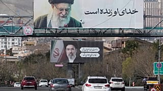 تسير المركبات تحت لوحات إعلانية تظهر صور المرشد الأعلى الإيراني الراحل آية الله علي خامنئي، في المقدمة، وابنه آية الله مجتبى خامنئي، خليفته